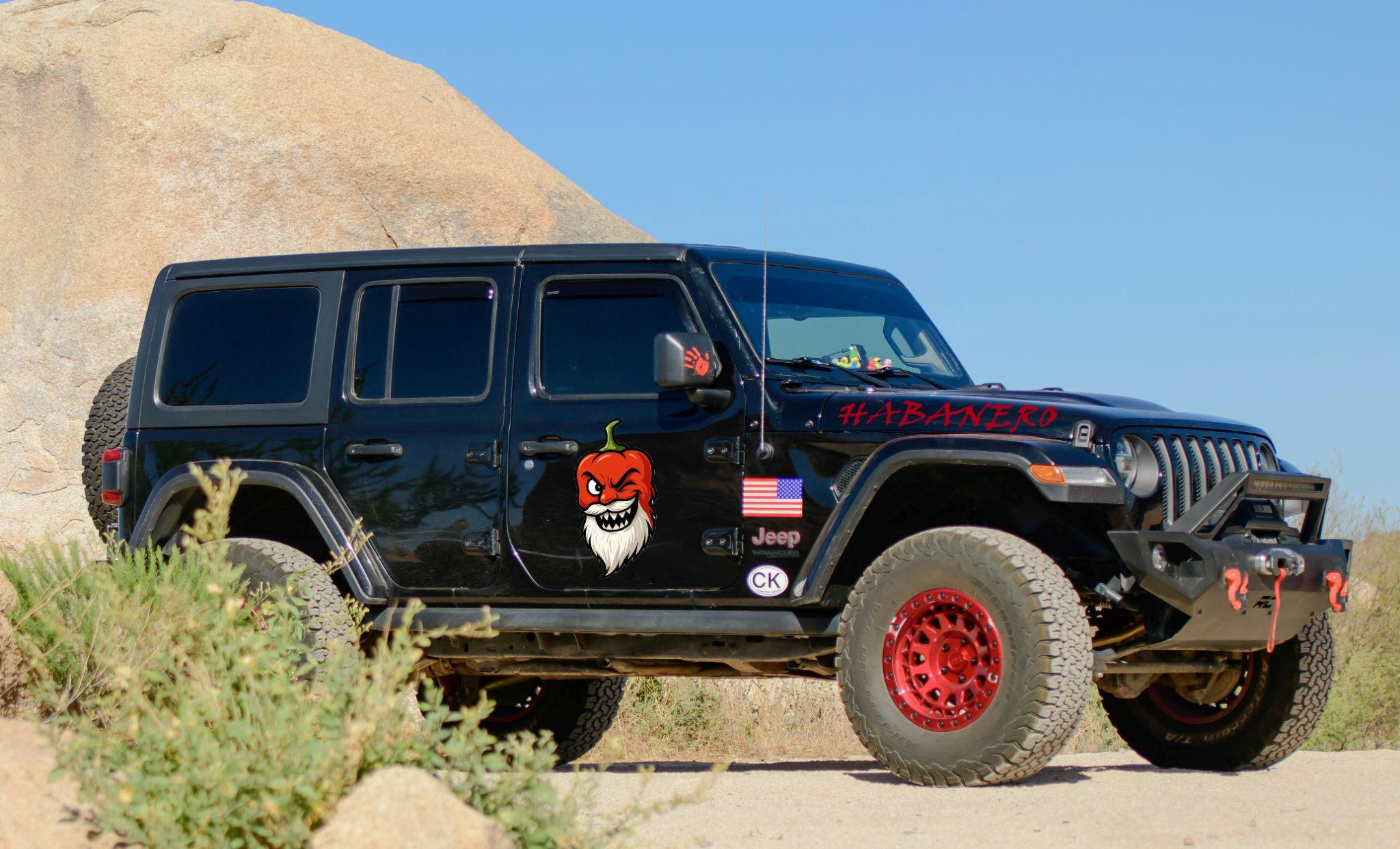 Black Jeep with red wheels, a pepper mascot decal and a red HABANERO hood decal parked beside a boulder in the desert